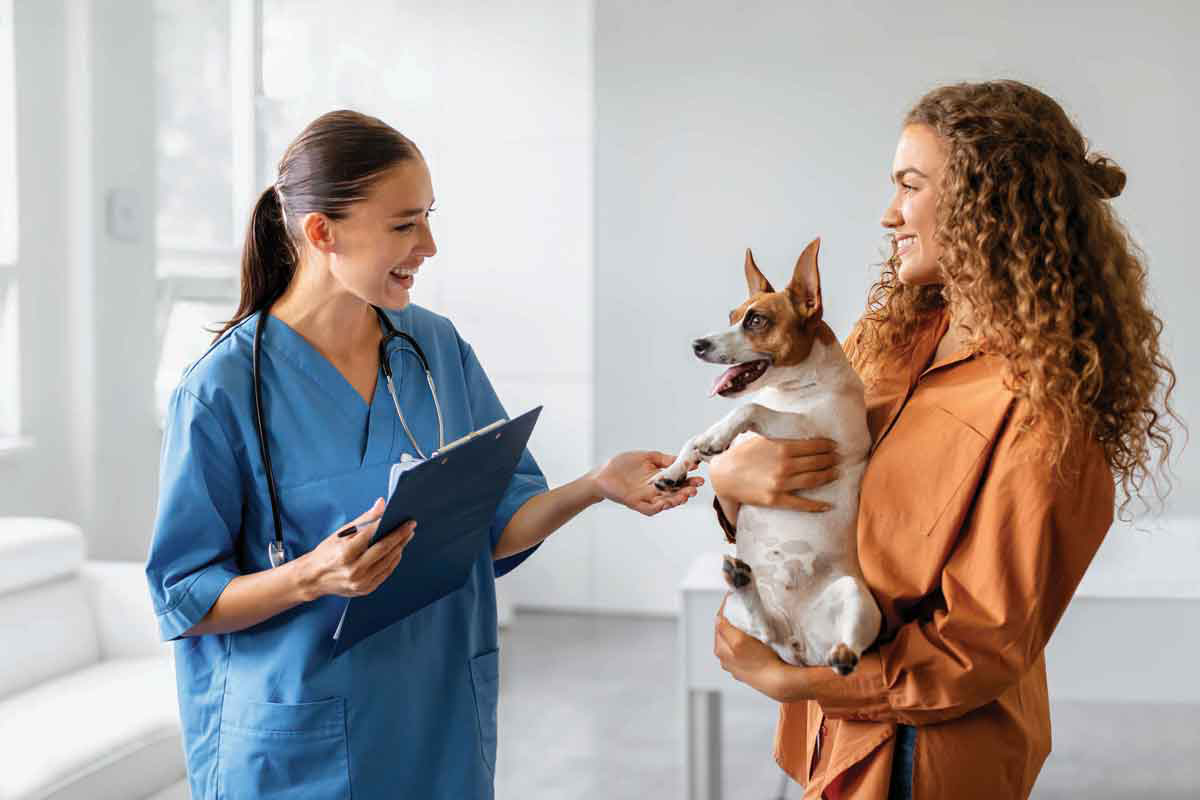 Una tecnica veterinaria tocca un cane, portato in braccio da una donna.